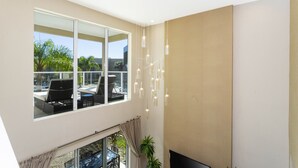 A modern living room with a large window, a flat-screen TV, and a ceiling light fixture. - Marvelous 4 Bd Close to Disney @ Magic Village 3153 (Kissimmee)