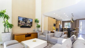 A modern living room with a white coffee table, grey sofas, and a large flat-screen TV mounted on the wall. - Marvelous 4 Bd Close to Disney @ Magic Village 3153 (Kissimmee)