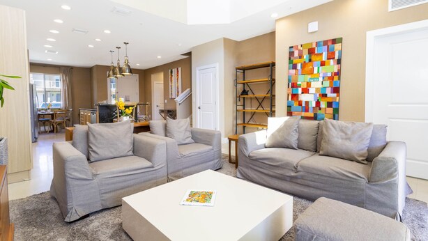 A modern living room with two grey sofas, a white coffee table, and a colorful abstract painting on the wall. - Marvelous 4 Bd Close to Disney @ Magic Village 3153 (Kissimmee)