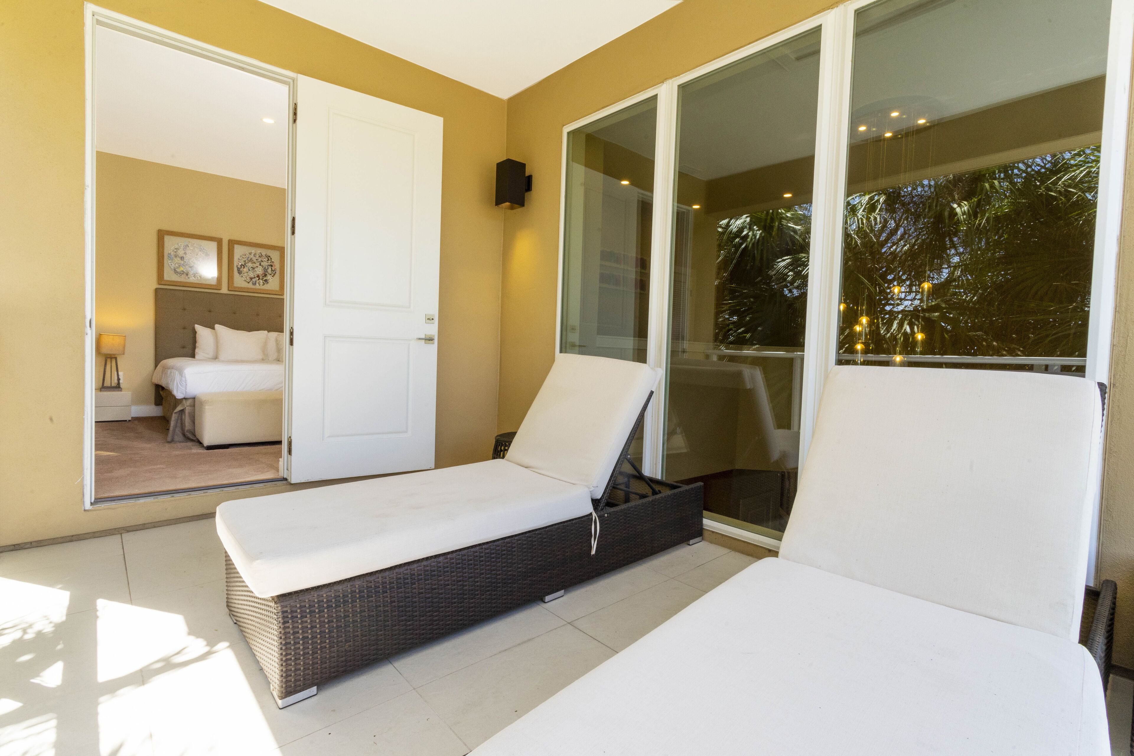 Una habitación con una cama, un sillón, un ventanal corredero y vistas a otra habitación con una cama y una mesita de noche.
