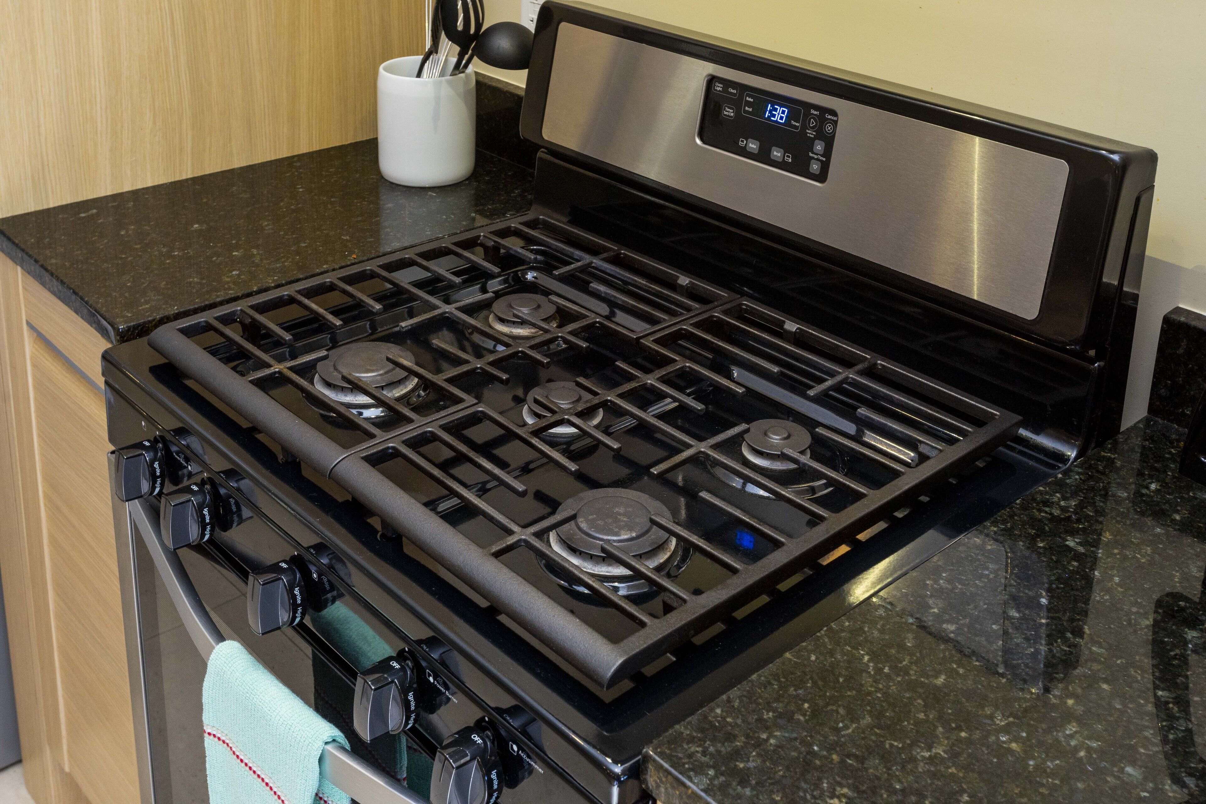 Une cuisine équipée d’une cuisinière en acier inoxydable, de plans de travail noirs et d’un récipient blanc contenant des ustensiles.