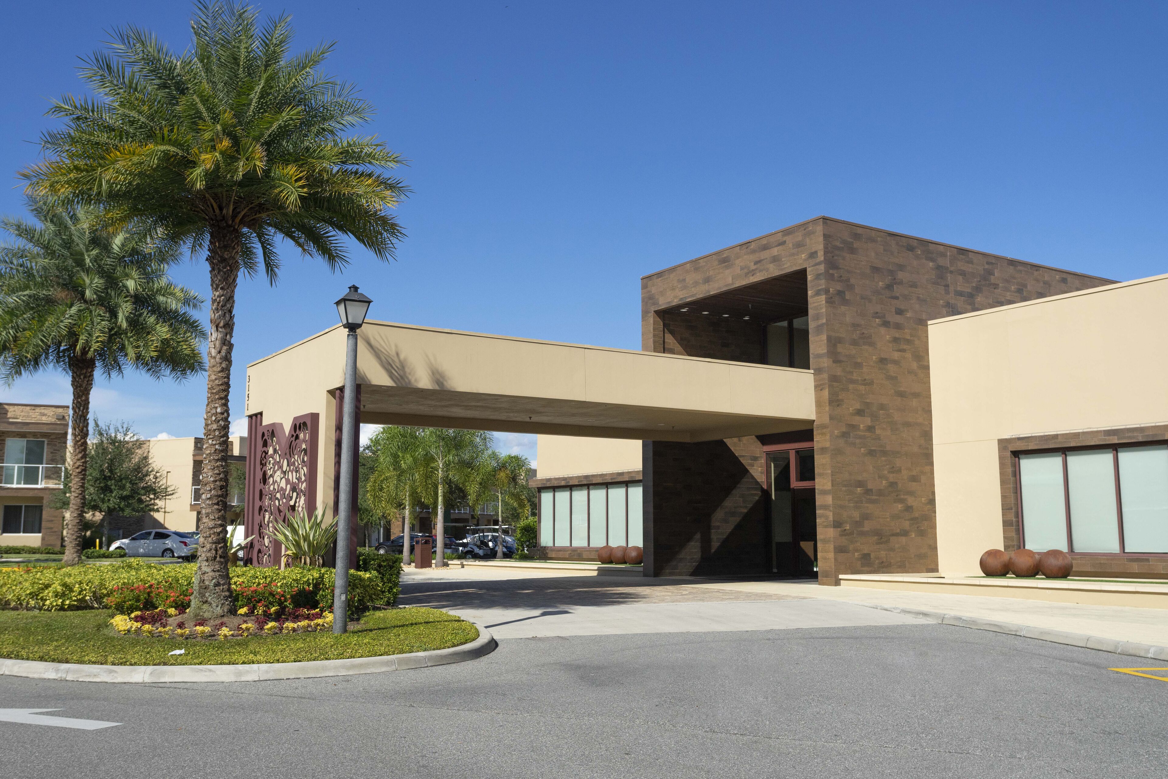 A modern building with a covered entrance, palm trees, and a clear blue sky.