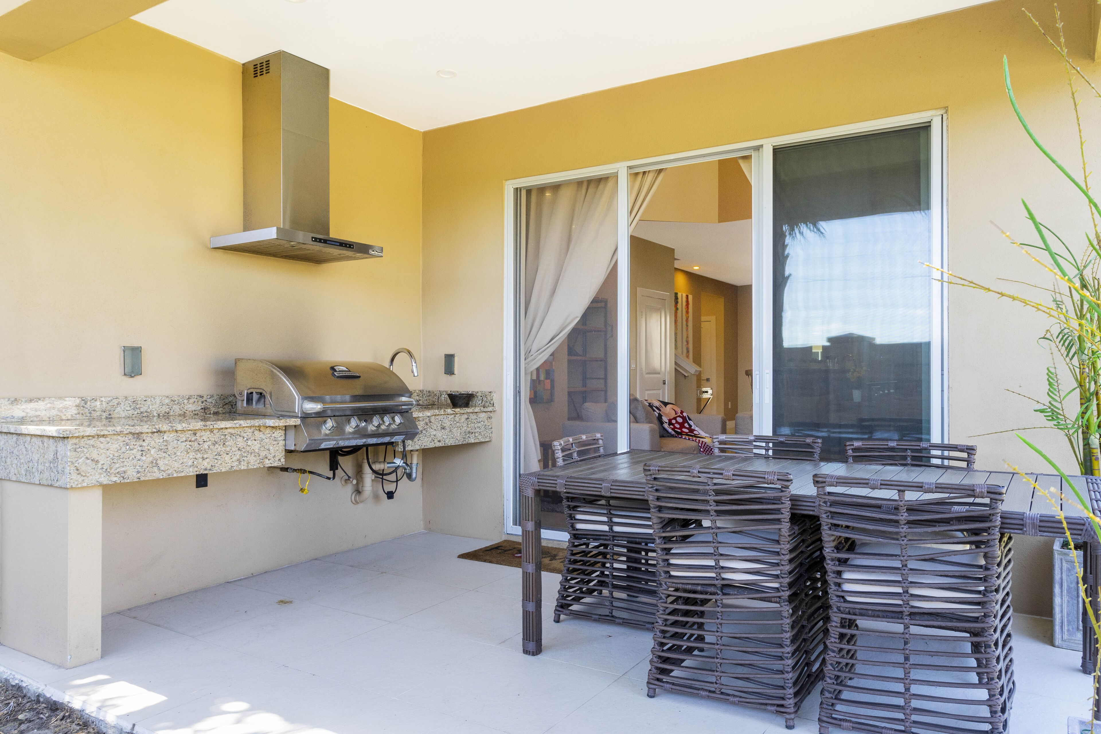 An outdoor kitchen with a grill, a dining table with chairs, and a sliding glass door leading to an interior space.