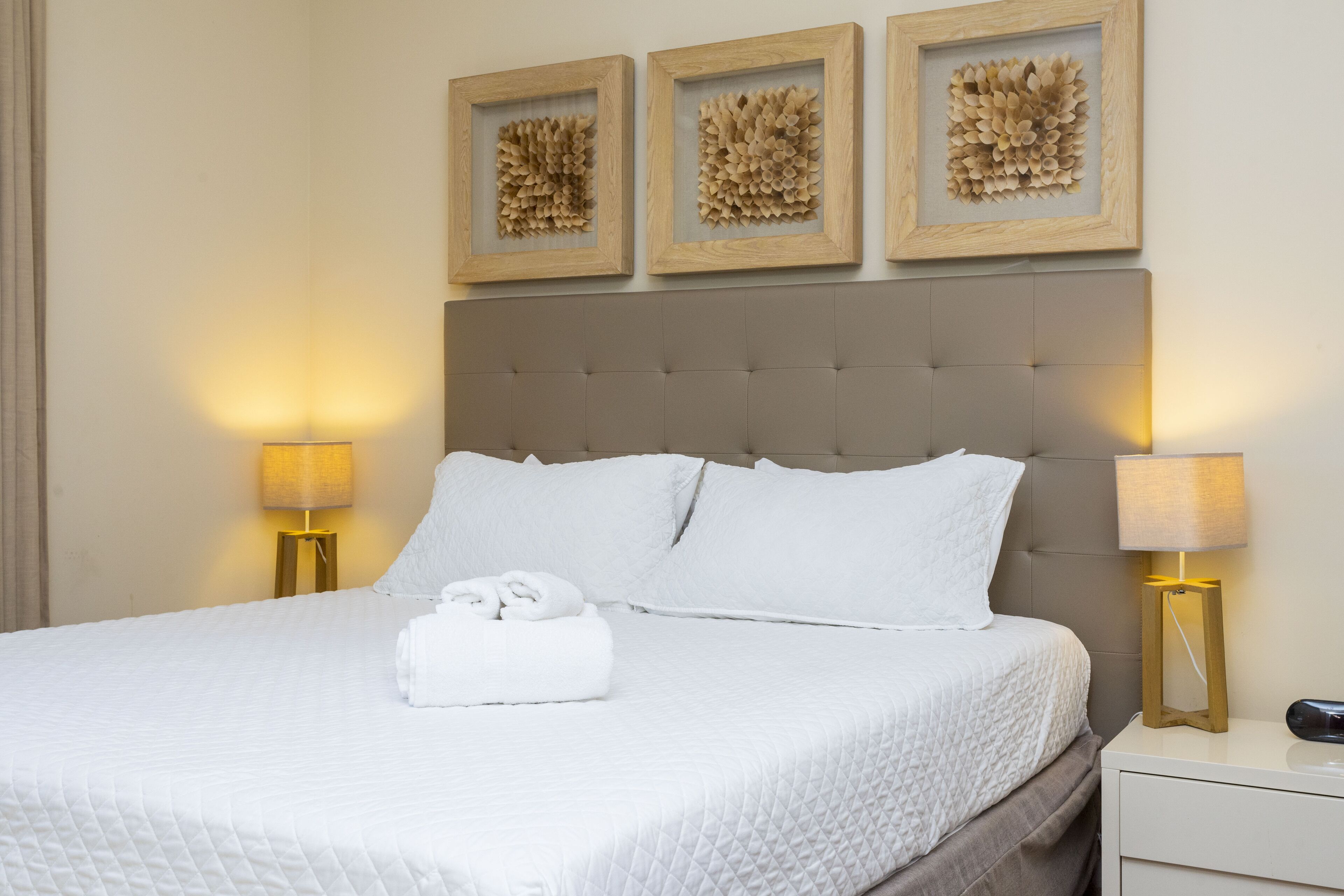 A neatly made bed with white bedding, a tufted headboard, and two bedside lamps.