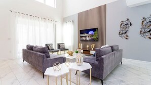 A modern living room with two grey sofas, a white coffee table, and a flat-screen TV mounted on the wall.