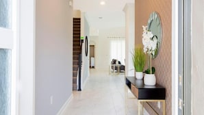 A modern hallway with a staircase, a console table with potted plants, and a large mirror on the wall.