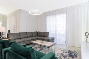 A modern living room with a sectional sofa, a coffee table, and a large window with sheer curtains.