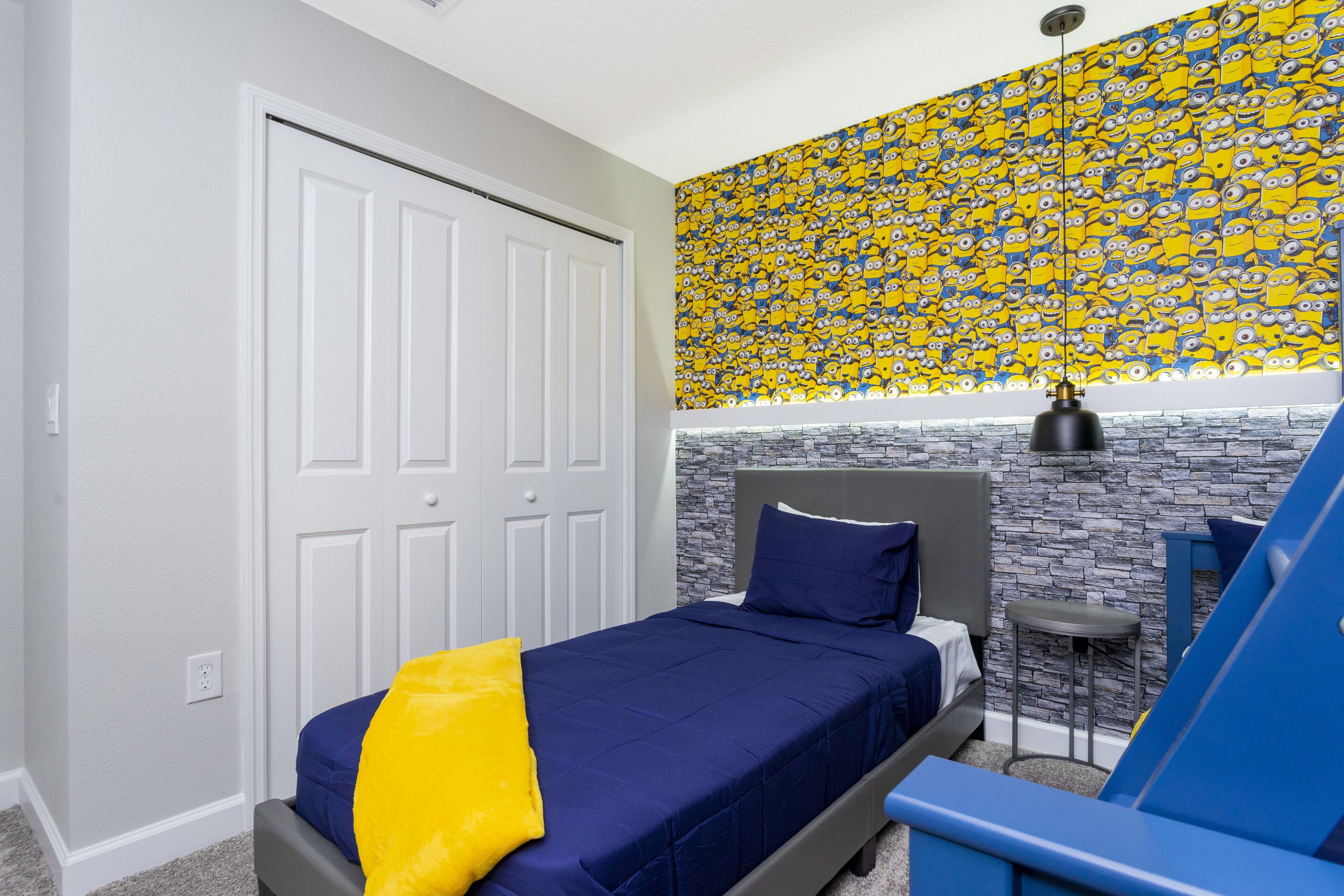 Una camera da letto con un letto, un comodino, una sedia, una parete decorata con i personaggi dei Minion e una parete a pietra.