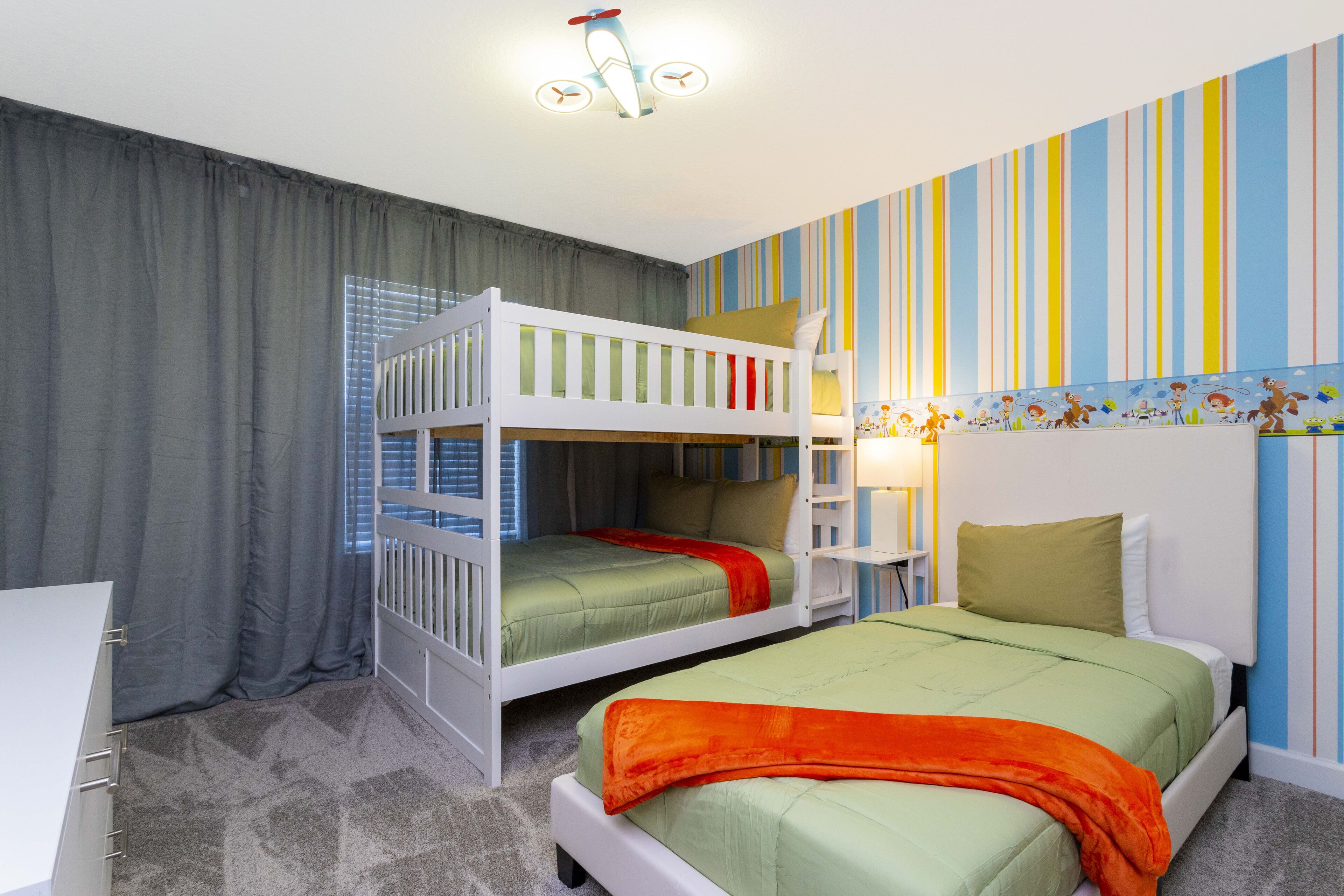 A bedroom with bunk beds, striped wallpaper, and a ceiling light fixture.