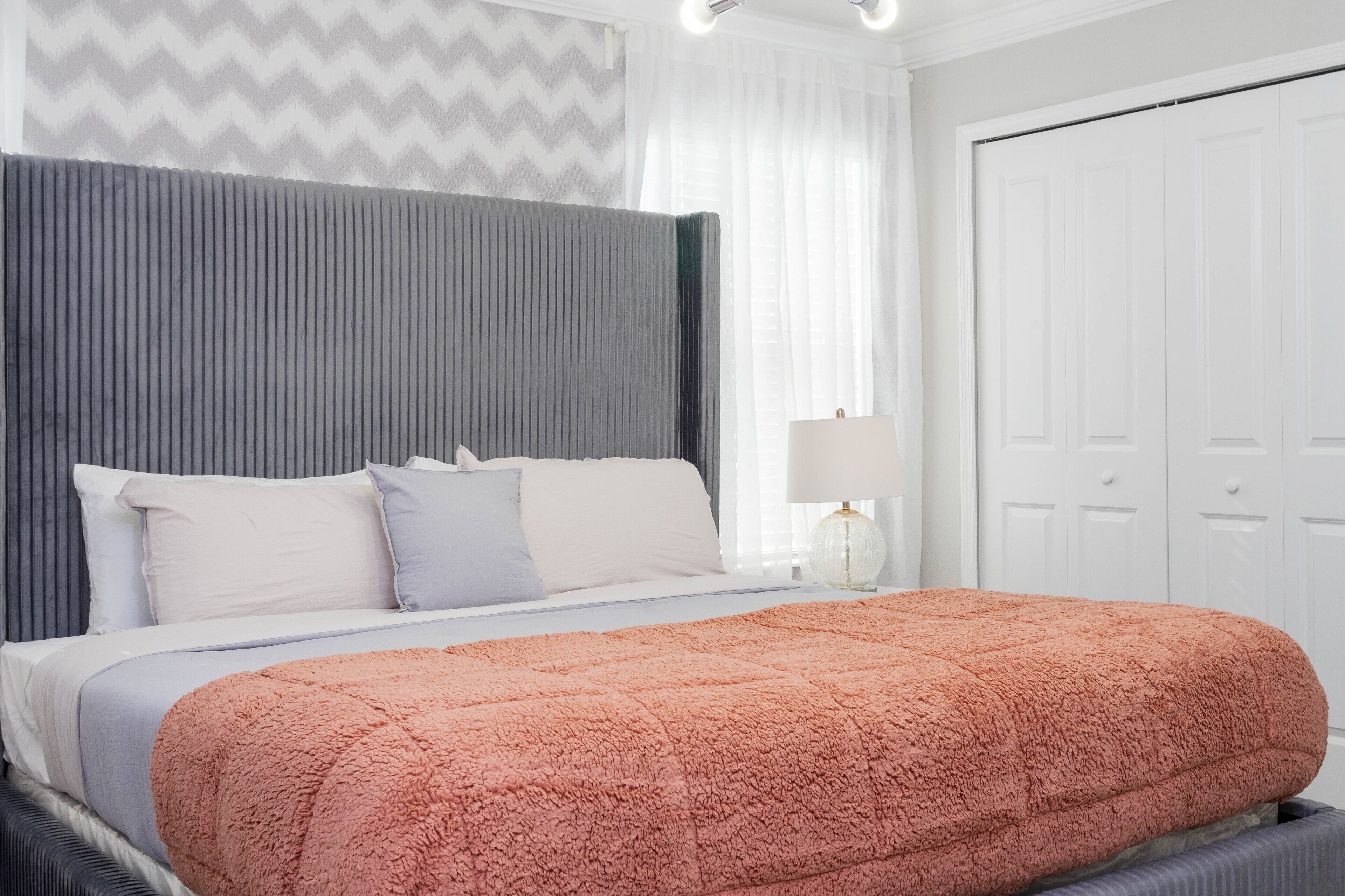 A neatly made bed with a fluffy pink blanket, a grey headboard, and white pillows.