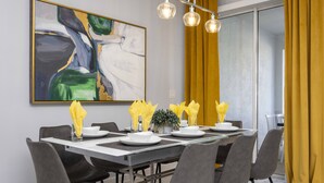 Een eetruimte met een moderne tafel voor zes personen, grijze stoelen en een groot abstract schilderij aan de muur.