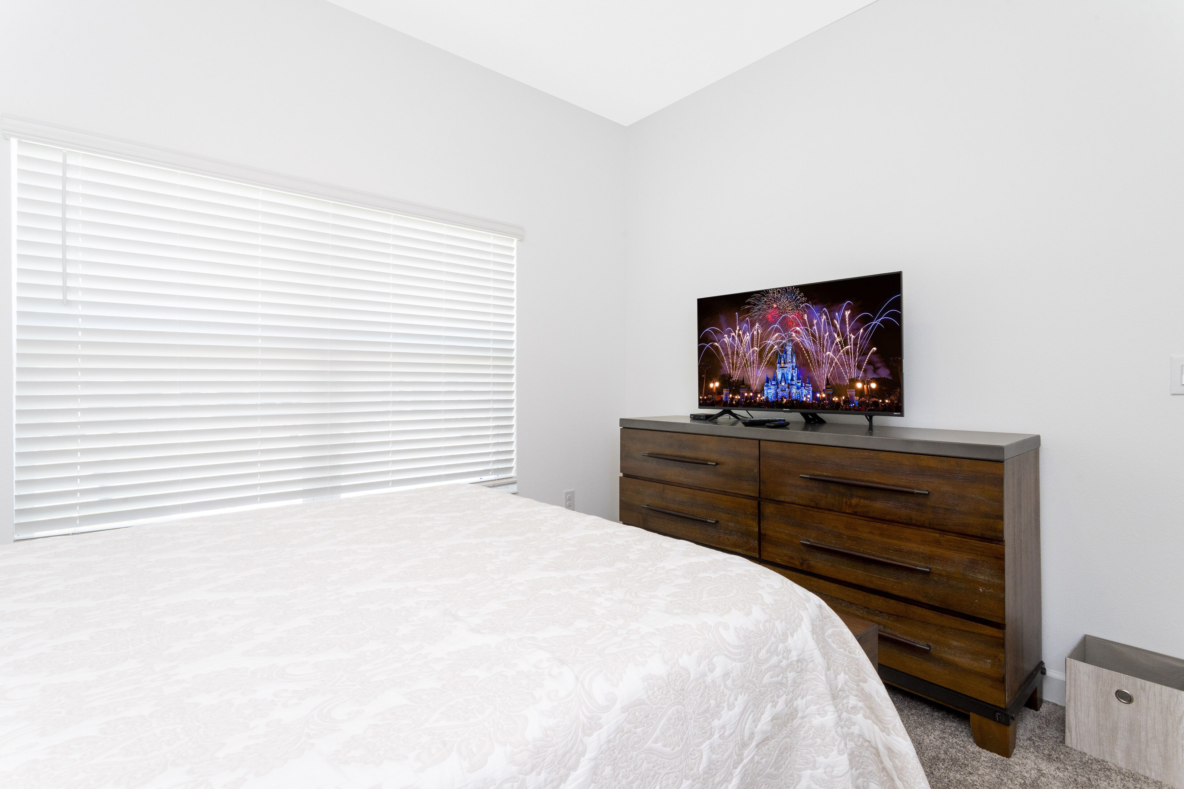 A bedroom with a bed, a dresser, and a television displaying fireworks.