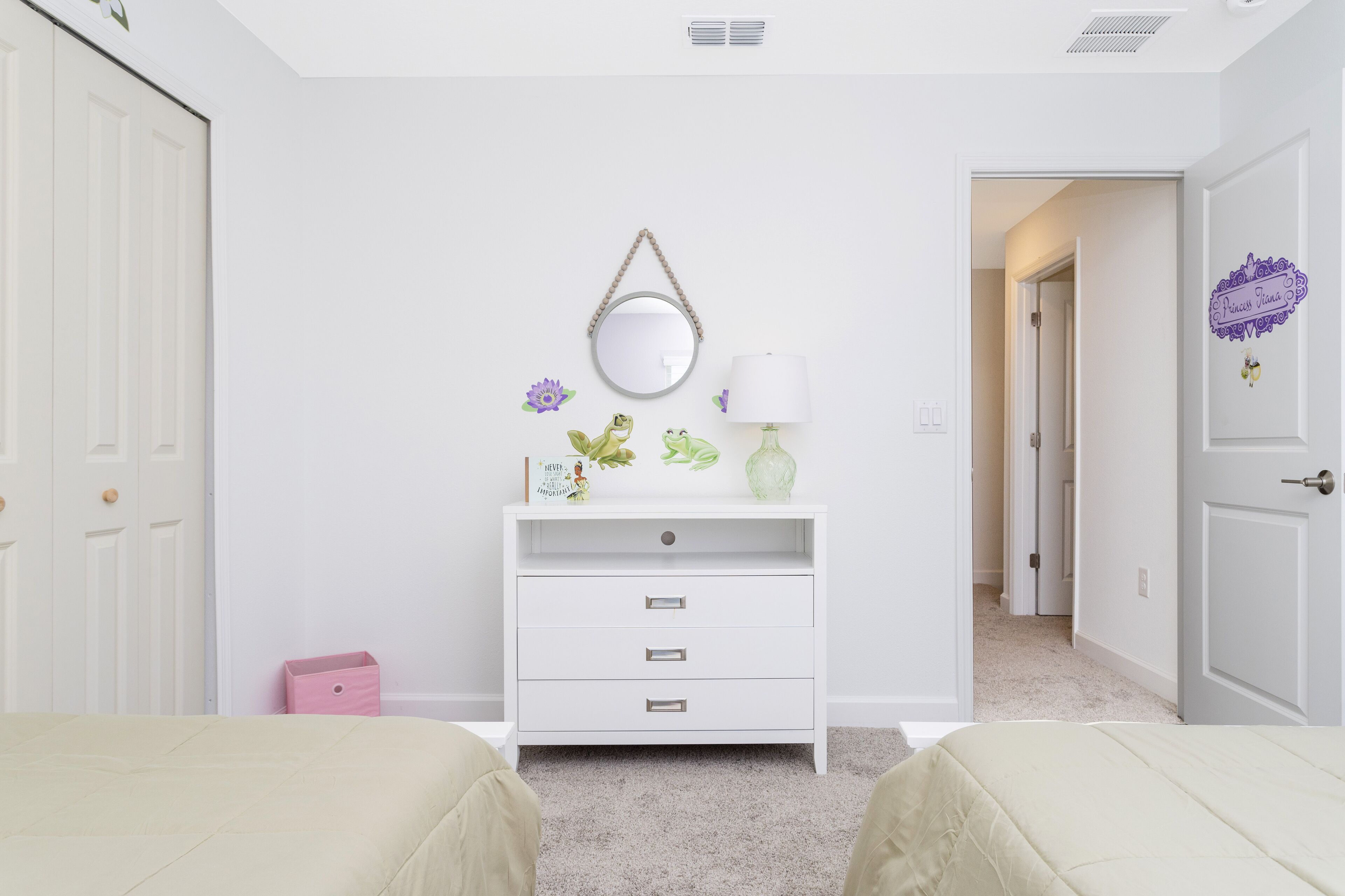 A bedroom with two beds, a white dresser with drawers, a mirror, and a small pink box.