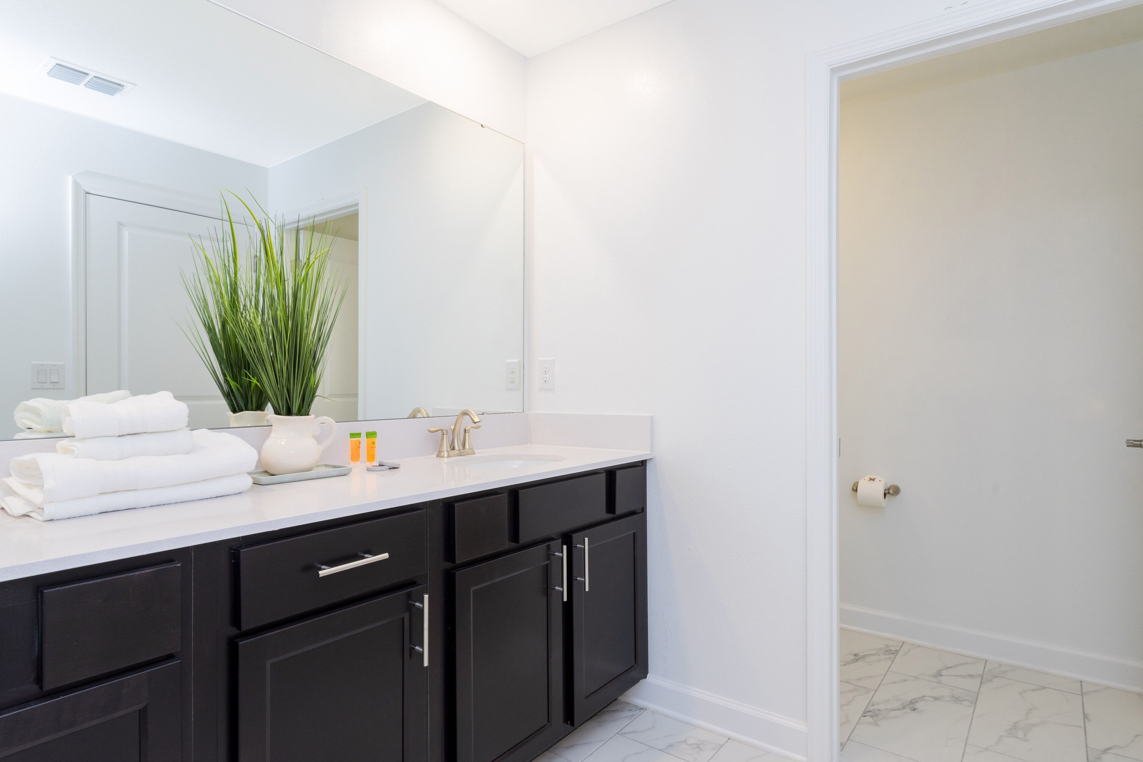 A modern bathroom with a white vanity, black cabinets, a large mirror, and a potted plant.
