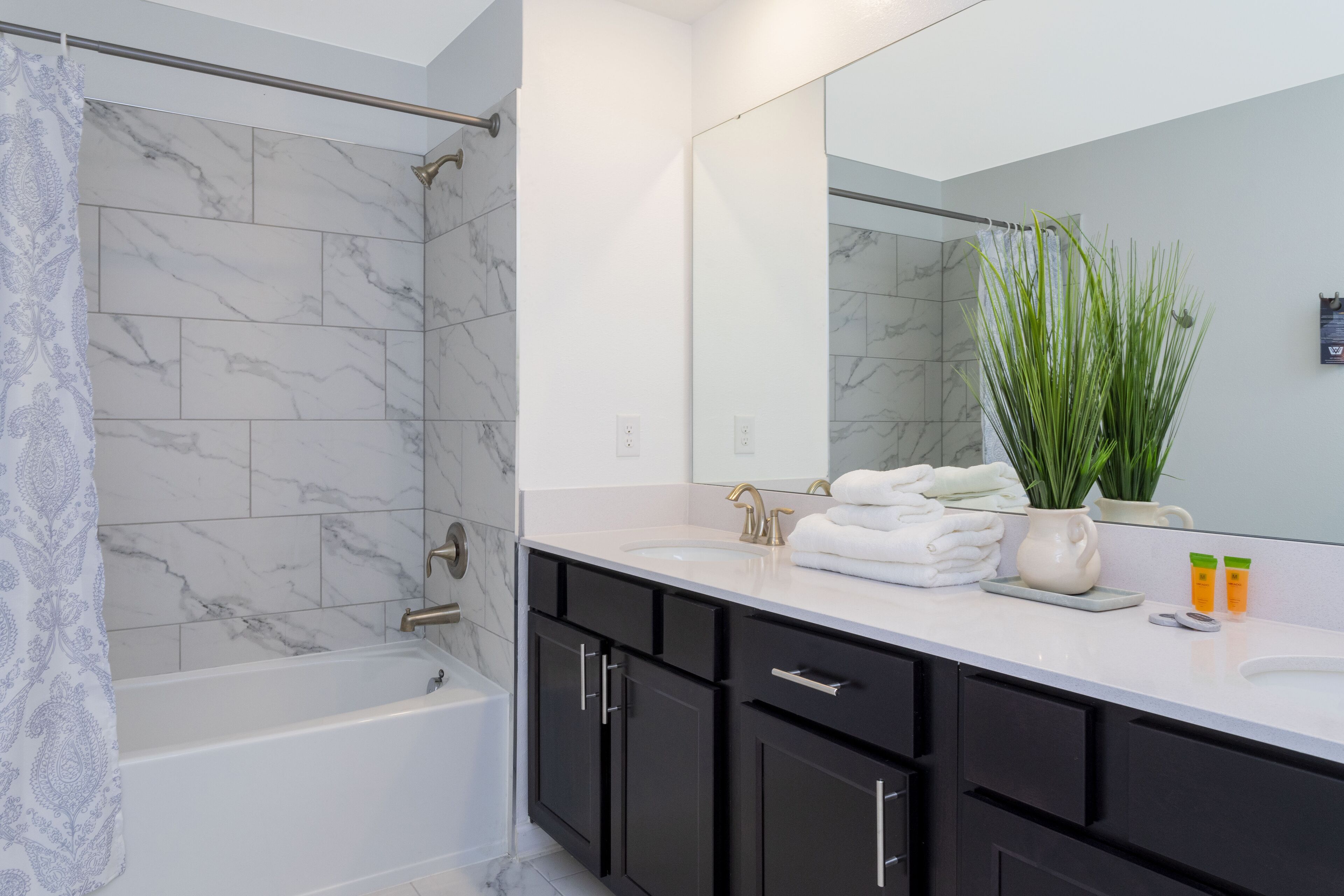 A modern bathroom with a bathtub, a large mirror, and a vanity with black cabinets.