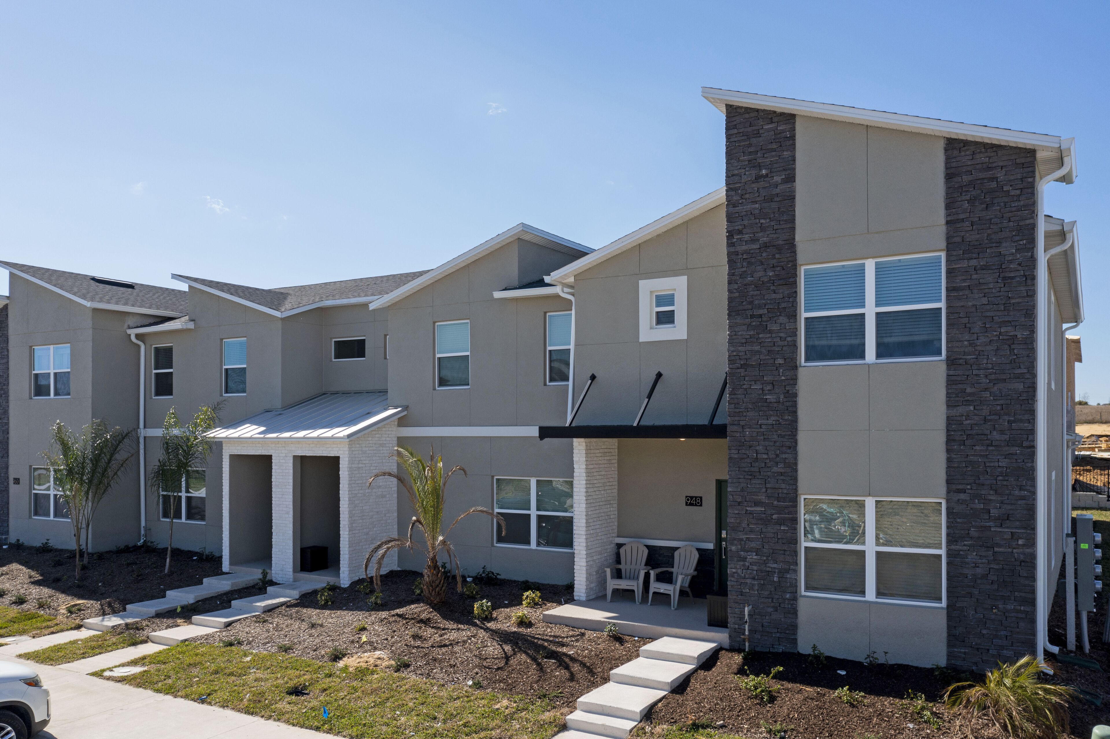 A modern multi-story residential building with a covered patio area, a small garden, and a visible address number.