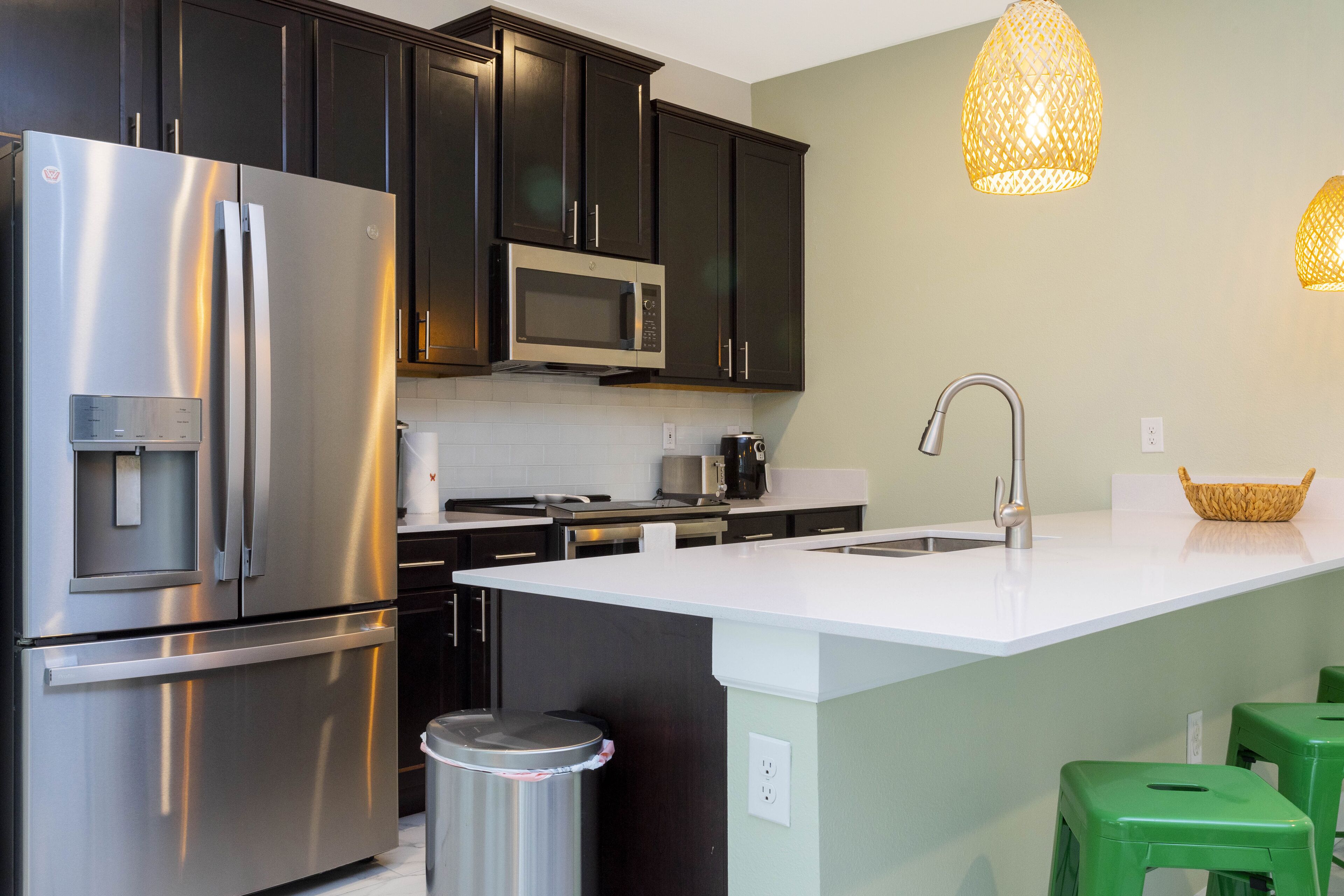 A modern kitchen with dark cabinets, stainless steel appliances, a white countertop island, and green bar stools.