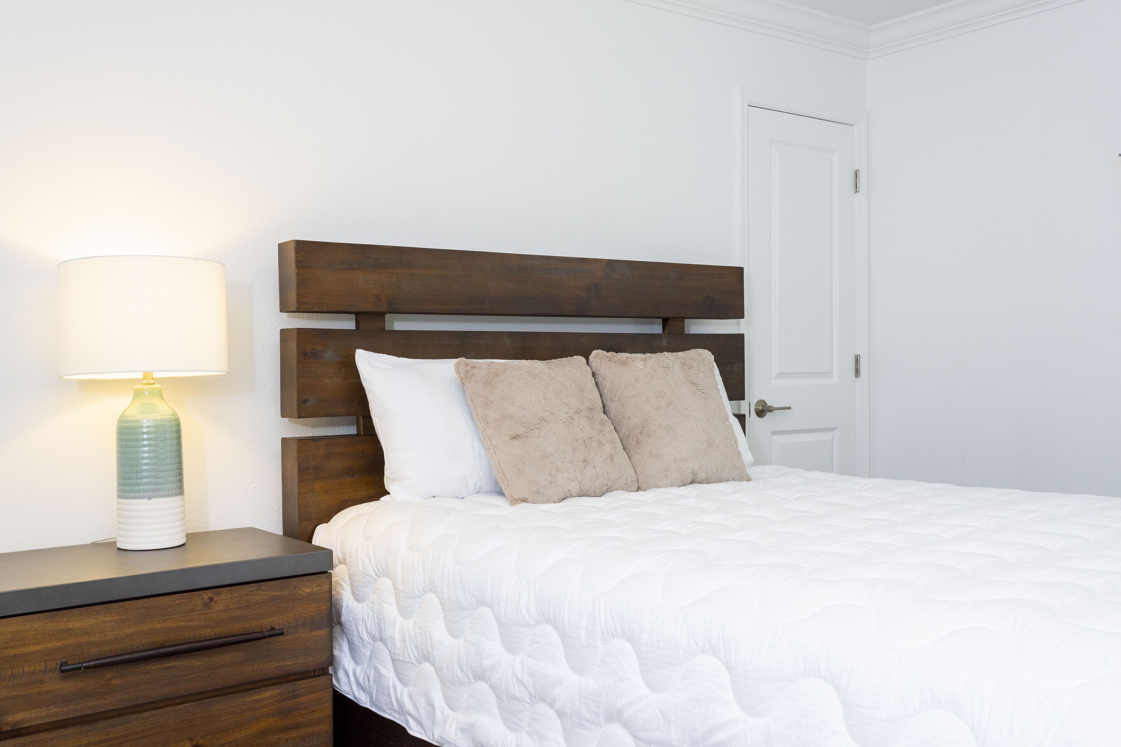Una cama bien hecha con cabecera de madera, una lámpara de noche y una mesita de noche con cajones.