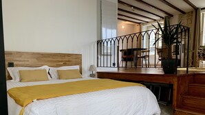 Un dormitorio con una cama grande, cabecera de madera y un área de escritorio con sillas y una planta en maceta.