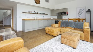 A modern living room with a sofa, ottoman, and a kitchen in the background. - Owl Lodge (Wedmore)