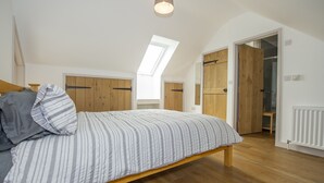 A bedroom with a bed, wooden wardrobe, skylight, and a door leading to another room. - Owl Lodge (Wedmore)