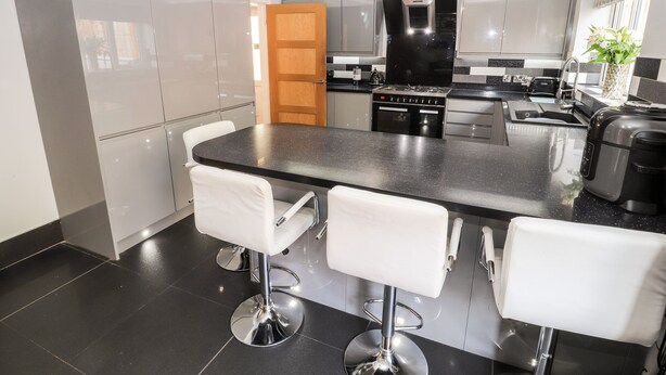 A modern kitchen with a central island, stainless steel appliances, and white bar stools. - Nant House (Wrexham)