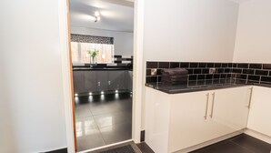 A modern kitchen with dark flooring, white cabinets, and a black countertop. - Nant House (Wrexham)