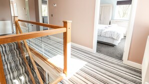A modern bedroom with a large bed, a wooden staircase, and a view of a bathroom. - Nant House (Wrexham)