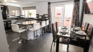 A modern kitchen with a central island, bar stools, and a dining table set for six. - Nant House (Wrexham)