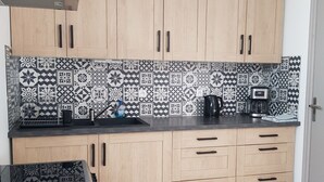 Cocina compacta con armarios de madera clara, encimera negra y azulejos decorativos en la pared.