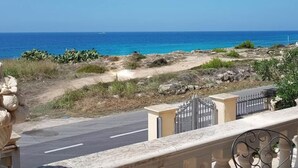 A coastal road with a clear view of the sea, a stone sculpture, and a gated entrance. - Villa della Libertà 10 Meters from the Sea, 10/12 SEATS, TORRE SUDA, Gallipoli (Torre Suda)