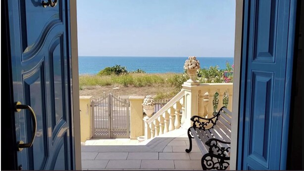 A view from a blue door to a balcony overlooking the sea, featuring a gate, a stone planter, and a bench. - Villa della Libertà 10 Meters from the Sea, 10/12 SEATS, TORRE SUDA, Gallipoli (Torre Suda)