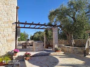 Un patio de piedra con pérgola, plantas en macetas y mobiliario de exterior.