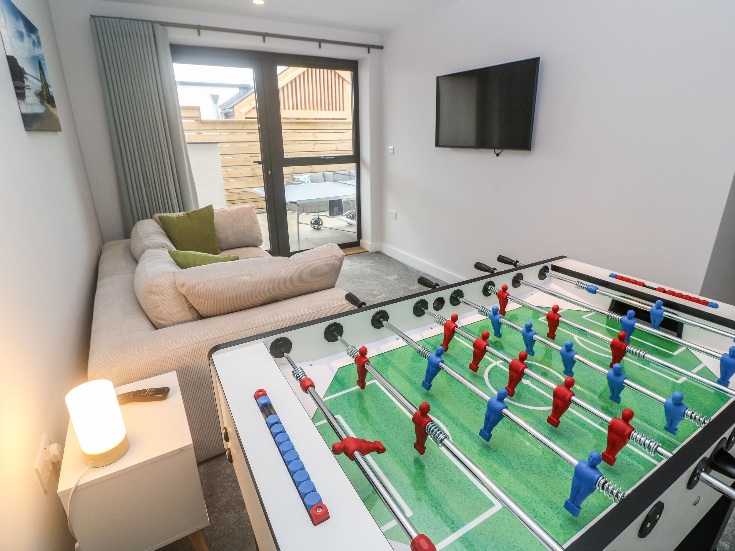 Une pièce comprenant un canapé, un baby-foot, une télévision et une fenêtre donnant sur un immeuble.