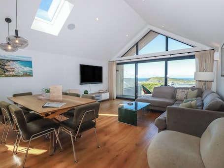 A modern living space with a dining area, a sofa, and large windows offering a view of the sea.