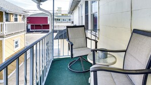 A balcony with two chairs and a small table, overlooking a building with a red awning and a parking area. - 1 Block to Convention Center! Dog-Friendly Apt (Wildwood)