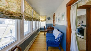 A narrow hallway with a blue sofa, wooden chairs, and a dining table. A kitchen with an oven and stove is visible through an open doorway. - Near Convention Center & Boardwalk! Apt w/ Sunroom (Wildwood)