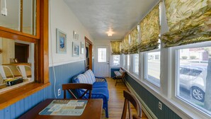 A room with a wooden table, blue sofa, and a window with floral curtains. - Near Convention Center & Boardwalk! Apt w/ Sunroom (Wildwood)