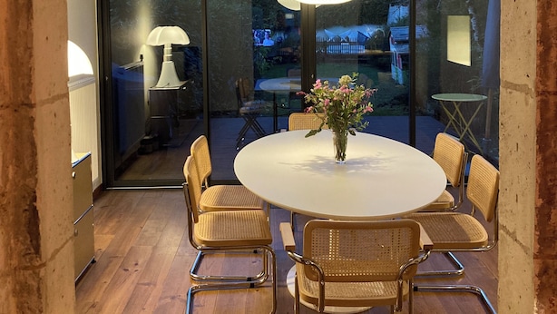 A modern dining area with a round table, wicker chairs, and a hanging light fixture. - Charming town house with pool and garden (Périgueux)