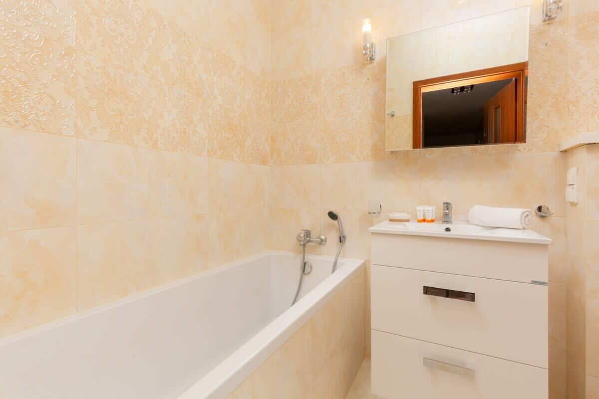 A bathroom with a bathtub, a vanity with drawers, a mirror, and toiletries.