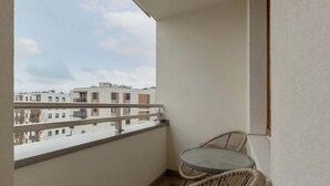 Un balcón con una mesa de vidrio y sillas de mimbre, con vista a una hilera de edificios.