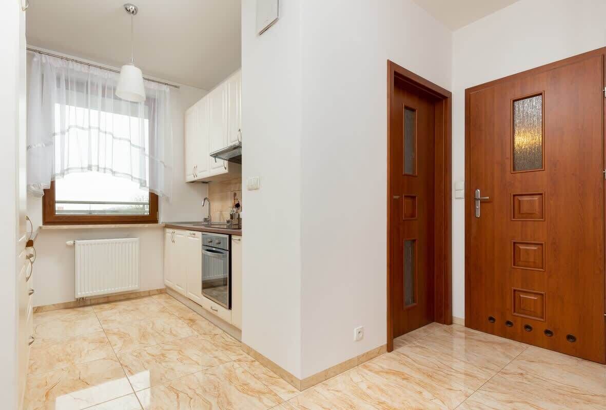 A kitchen with white cabinets, a window with sheer curtains, a wooden door, and a radiator.