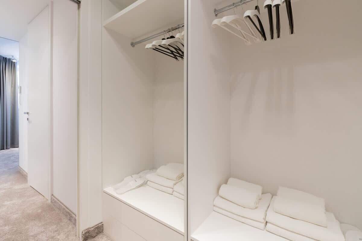 Habitación de hotel con un espejo grande, una cama bien tendida, un toallero y una puerta visible que da a otra habitación.