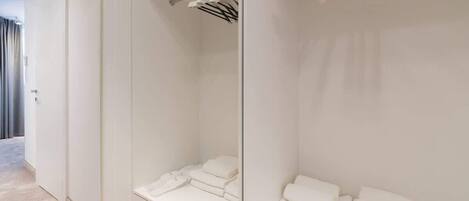 Habitación de hotel con un espejo grande, una cama bien tendida, un toallero y una puerta visible que da a otra habitación.