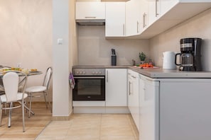 A compact kitchen with white cabinets, a built-in oven, a coffee maker, and a dining area with chairs and a table. - Tasteful Apartment | Balcony | 750 m to the beach (Łukęcin)