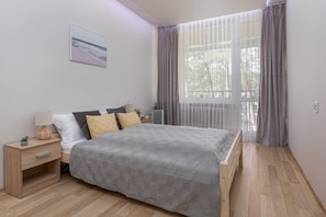 A neatly arranged bedroom with a bed, bedside table, lamp, and a window with curtains. - Tasteful Apartment | Balcony | 750 m to the beach (Łukęcin)