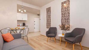 A modern living room with a grey sofa, two armchairs, a small table, and a kitchen in the background. - Tasteful Apartment | Balcony | 750 m to the beach (Łukęcin)