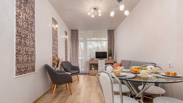 A modern living room with a glass dining table, grey sofas, and a TV. - Tasteful Apartment | Balcony | 750 m to the beach (Łukęcin)