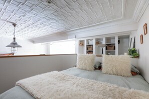 Une chambre avec un plafond blanc, un lit agrémenté de coussins moelleux, une lampe suspendue et une fenêtre donnant sur un beau paysage.