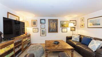 A living room with a TV, sofa, coffee table, and various framed pictures on the wall.